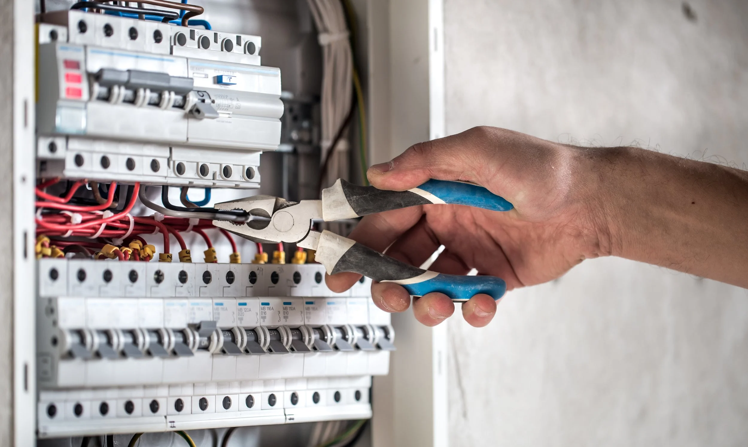 Une main utilise une pince pour manipuler des fils électriques dans un panneau électrique.