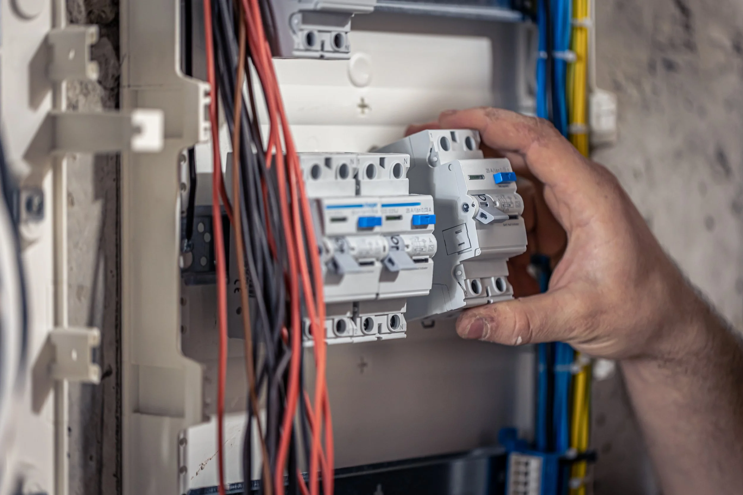 Une main manipulant un disjoncteur électrique dans un panneau électrique.