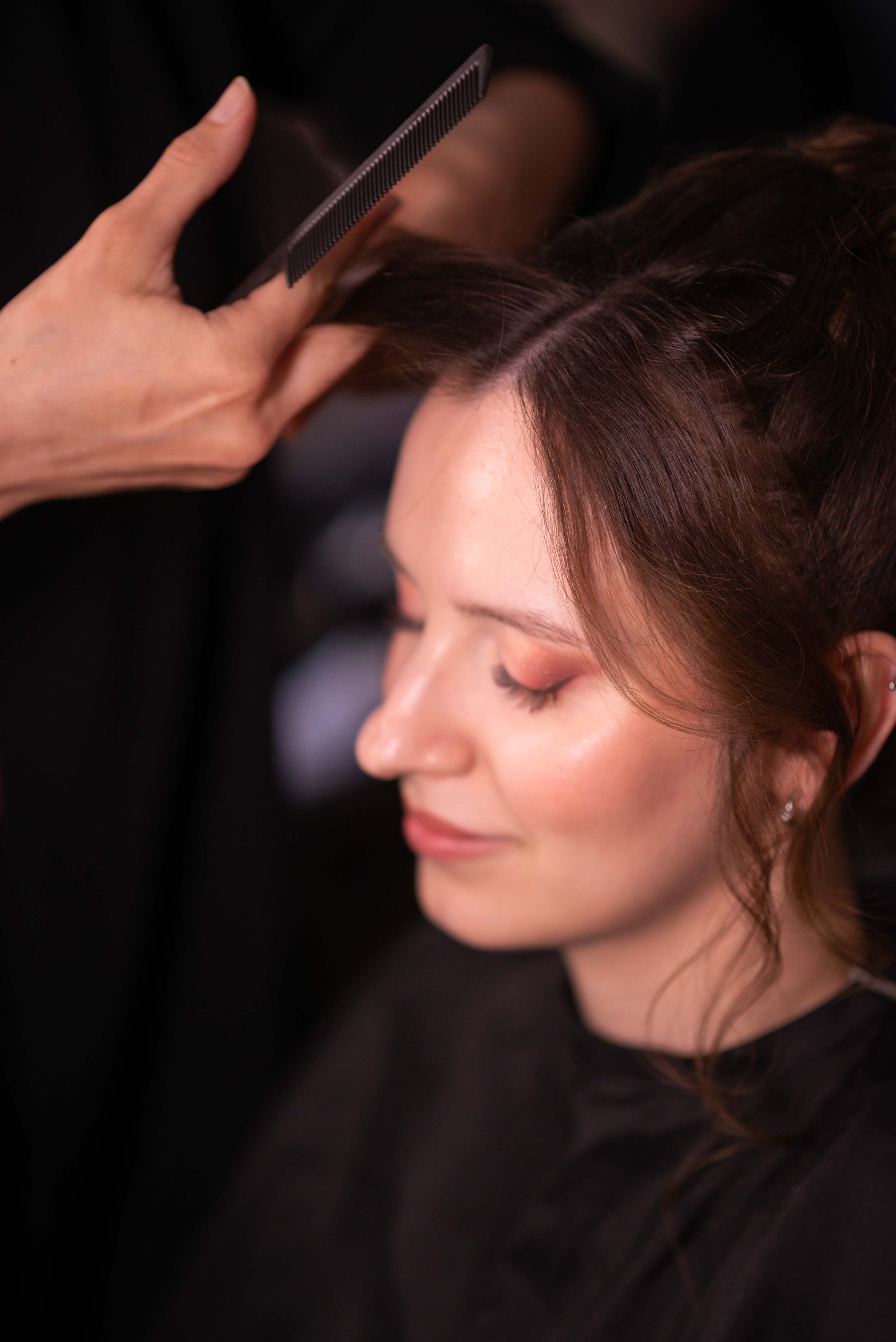 Frisörin/Stylistin frisiert eine Braut mit braunen Haaren, die mit geschlossener Augen entspannt.