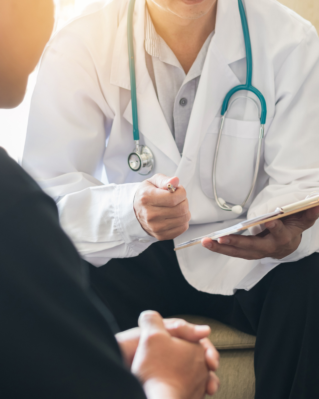 Doctor in white coat with stethoscope consulting with a patient, holding a clipboard and pen.