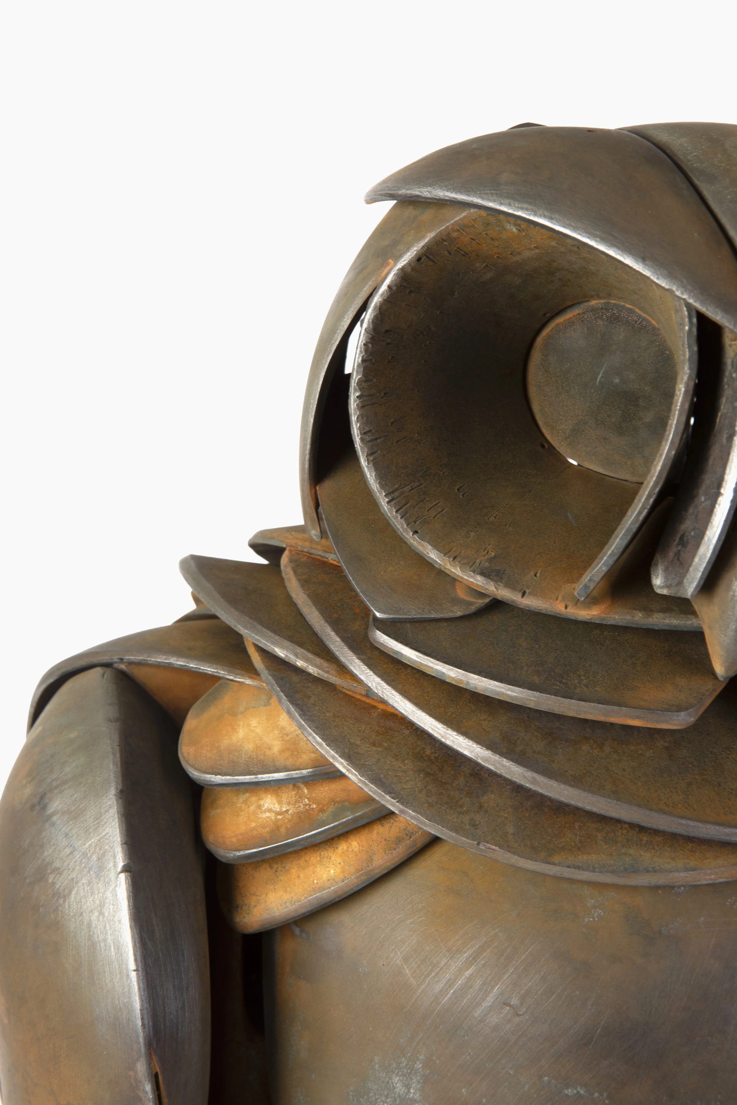 Close-up of a metallic sculpture resembling a stylized animal, with layered, curved, and textured metal pieces forming a head and neck, set against a plain white background.