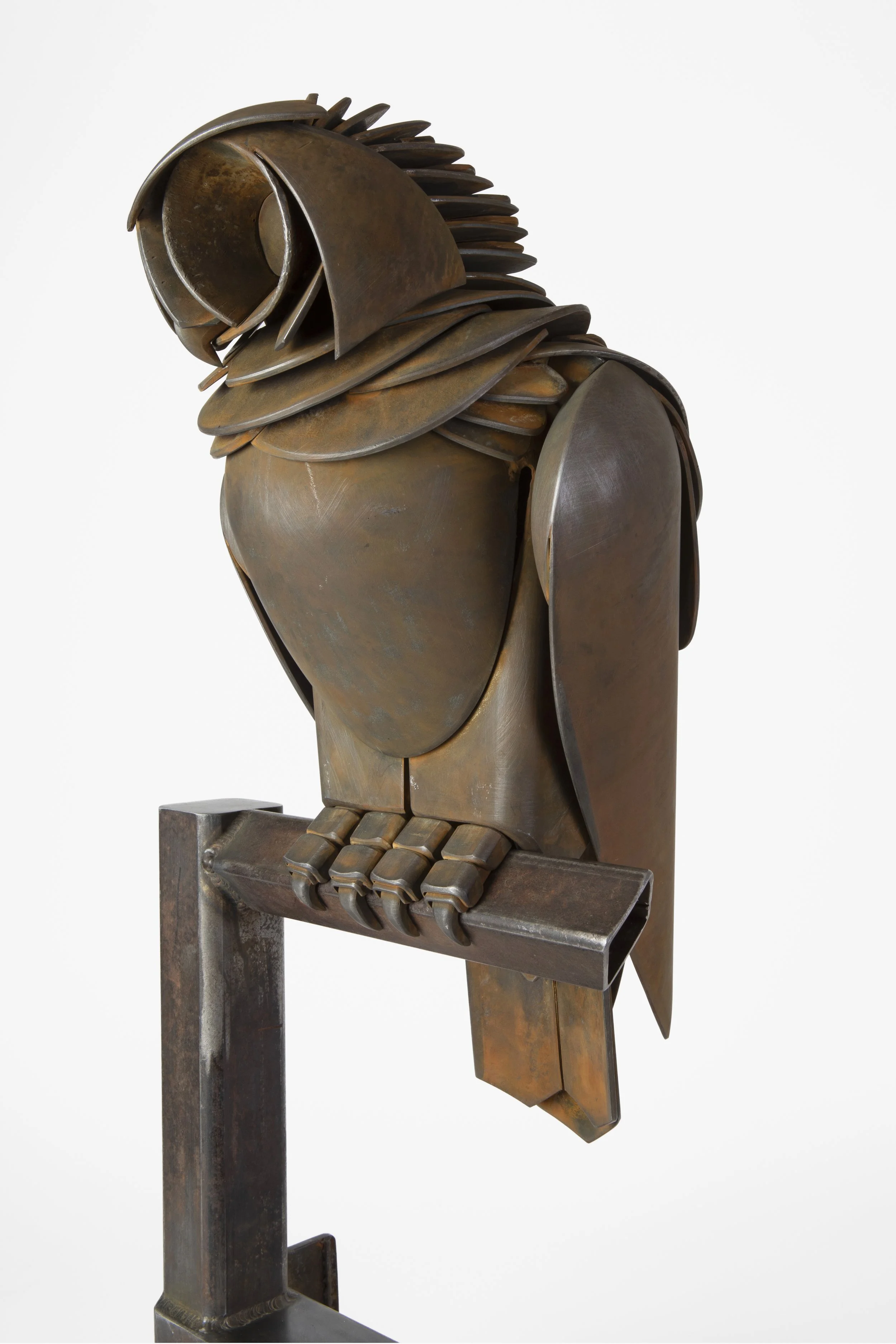 A bronze sculpture of an owl sitting on a rectangular base and a horizontal perch, with layered feathers on the head and body, made of curved metal plates.