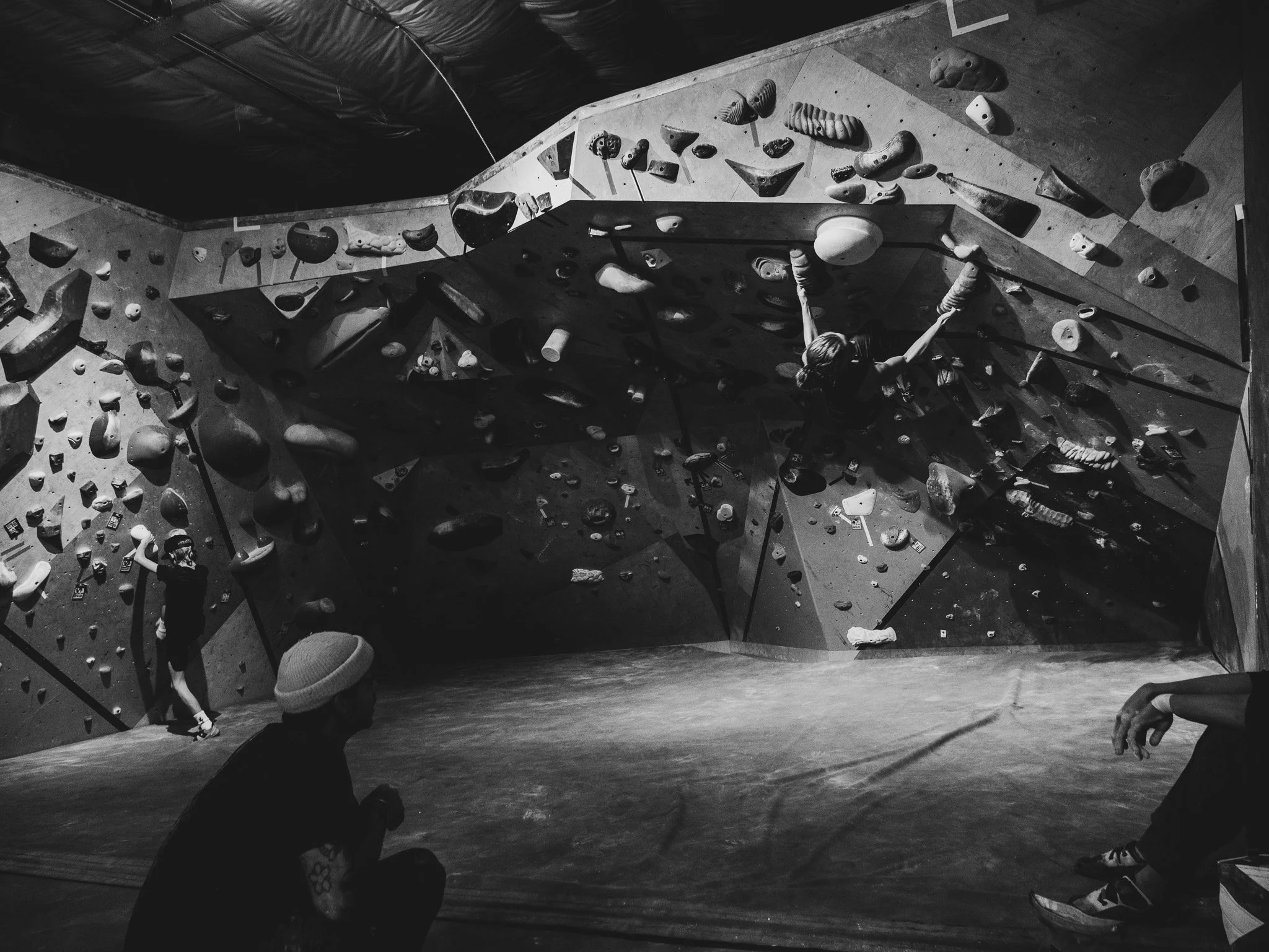 People indoor bouldering at a climbing gym with various holds on the wall.