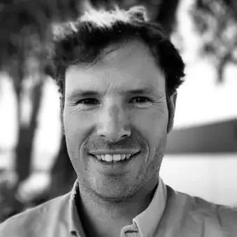 A black-and-white photo of a smiling man with short, dark hair outdoors.
