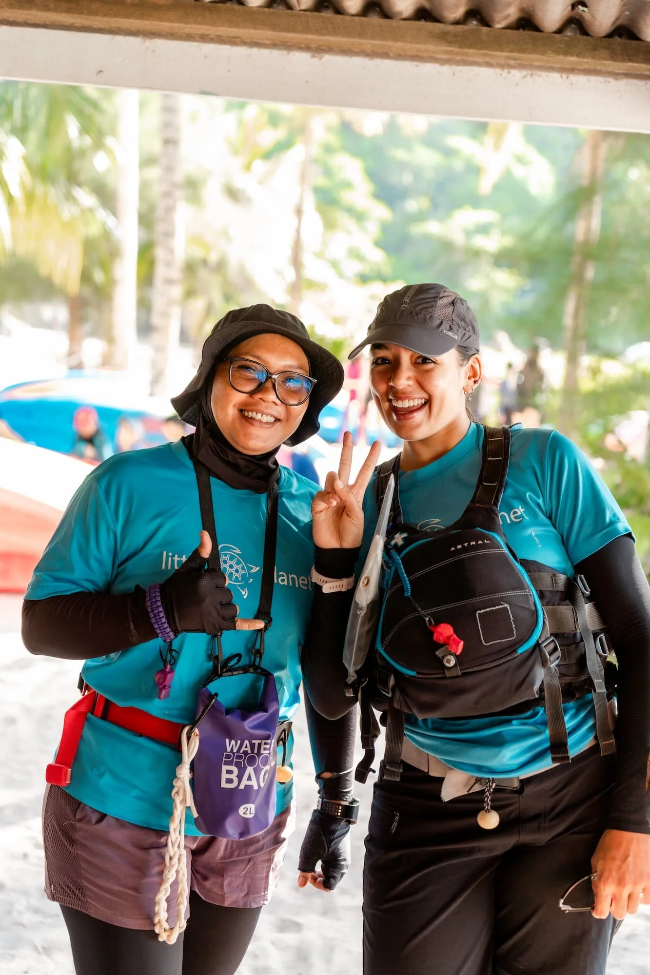 Two women smiling outdoors, wearing athletic clothes and hats, with a lush green background and trees.
