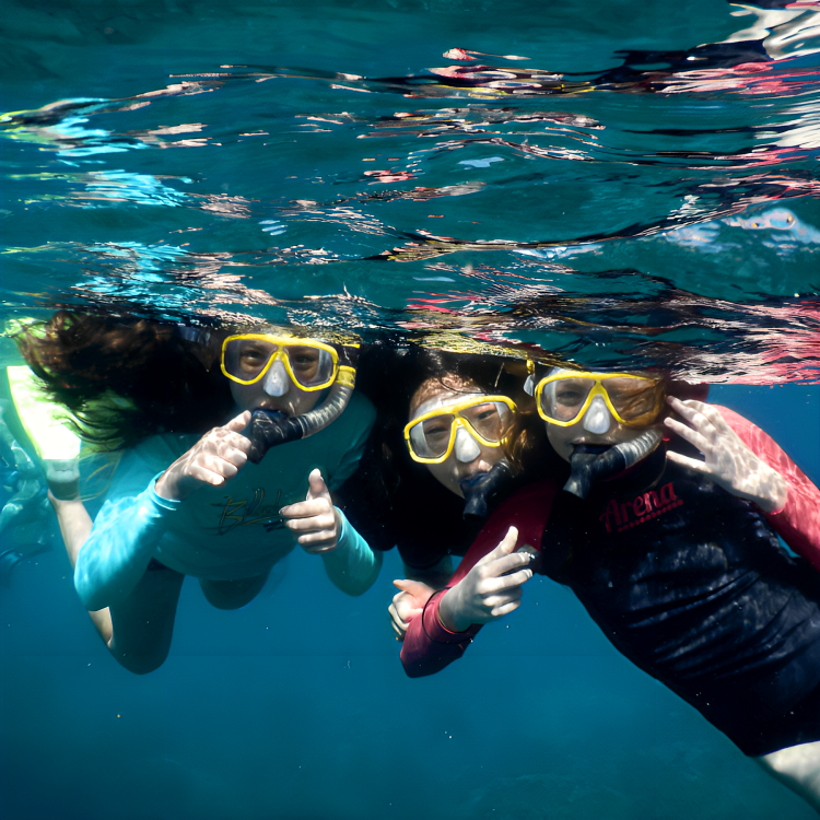 Three children wearing snorkeling masks and snorkels underwater, posing for a photo.