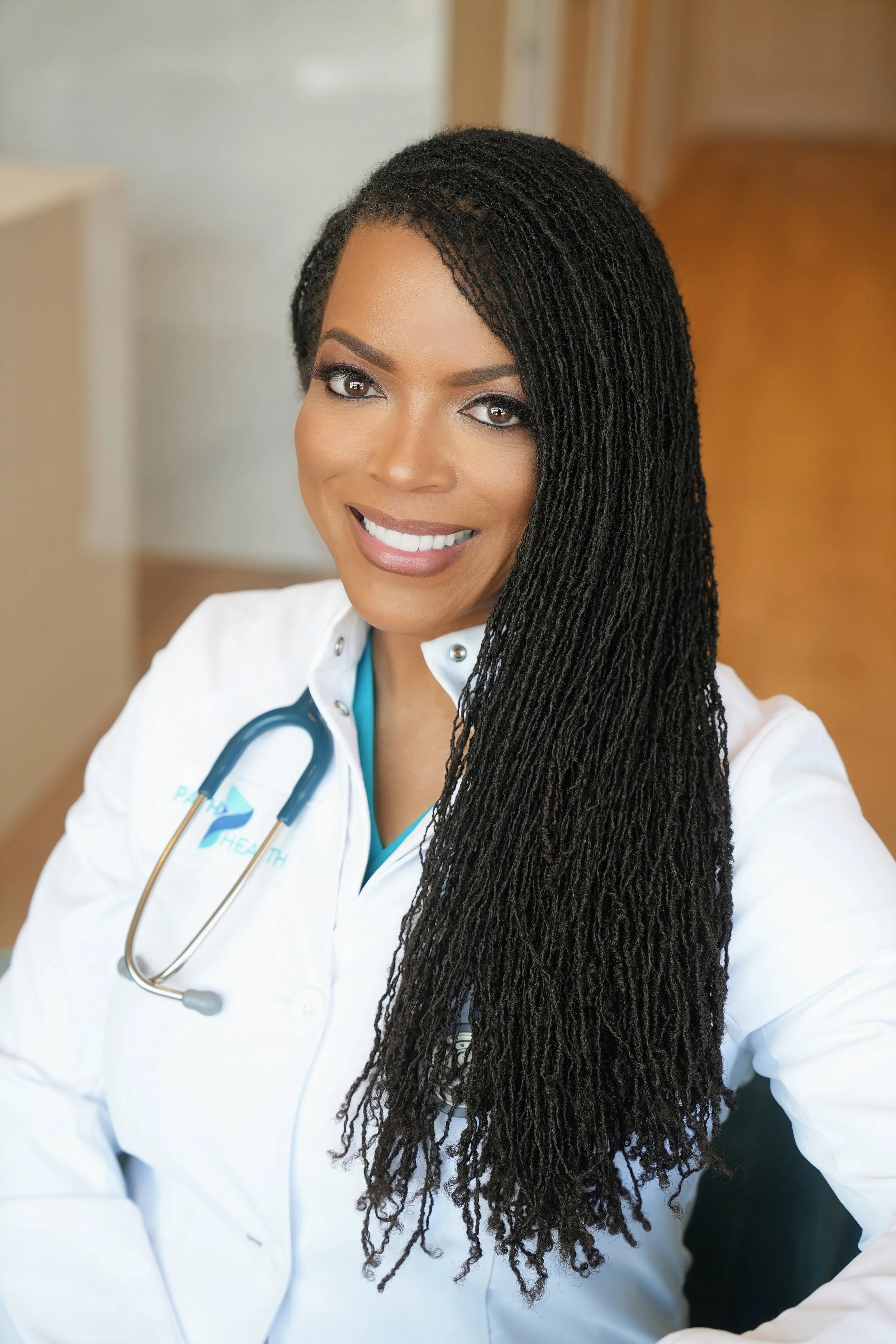 A woman healthcare professional smiling and wearing a white medical coat with a stethoscope around her neck.