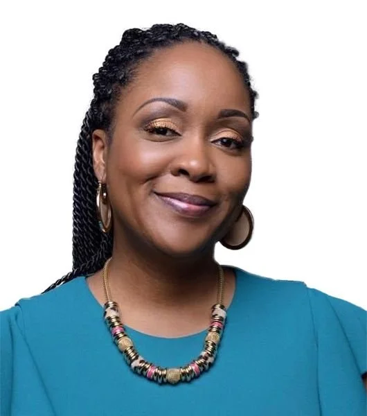 A smiling African American woman with braided hair, wearing a turquoise dress, gold hoop earrings, and a colorful beaded necklace.