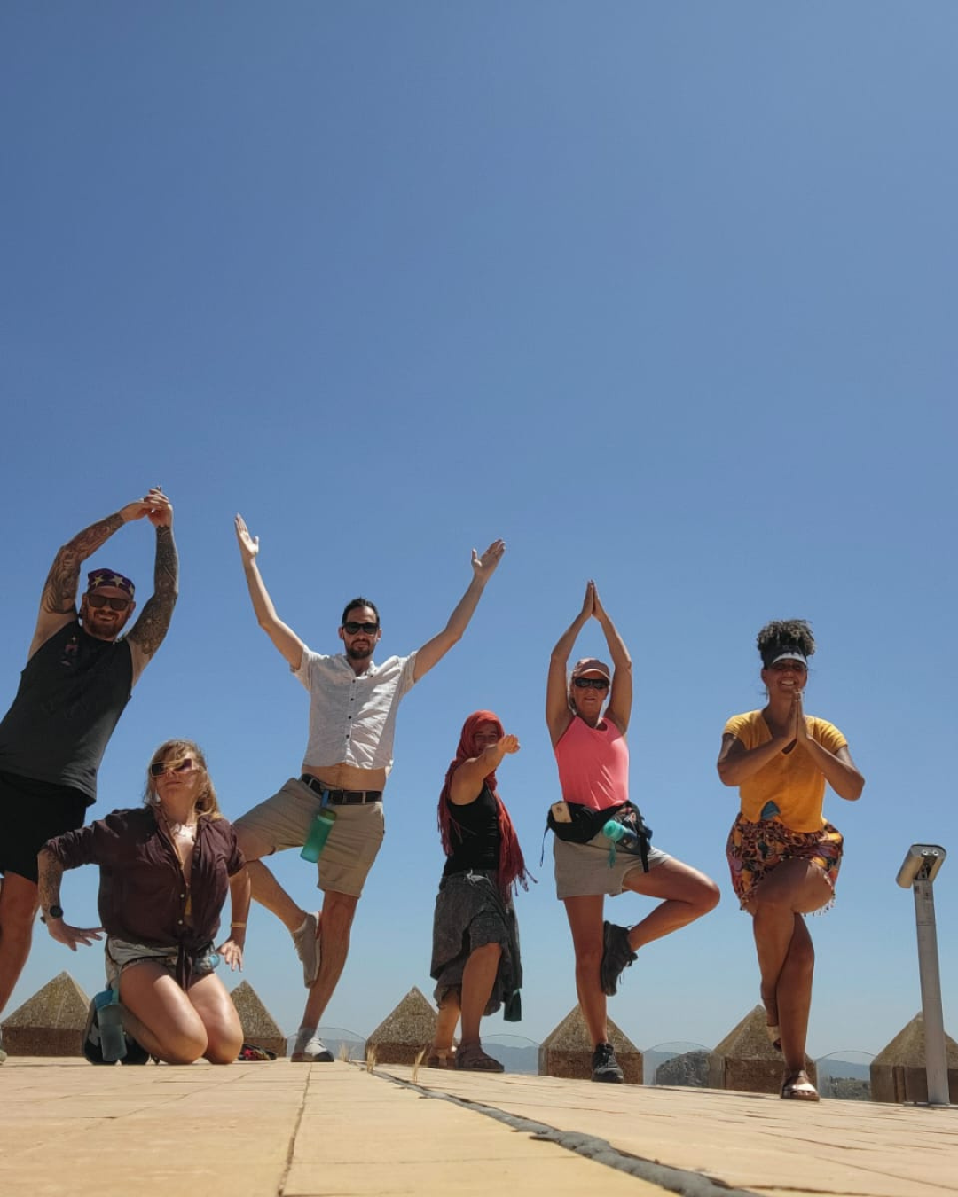 Group of six people performing yoga poses outdoors under a clear blue sky.