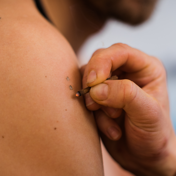 Close-up of a hand using a needle to tattoo a design on a person's upper arm.
