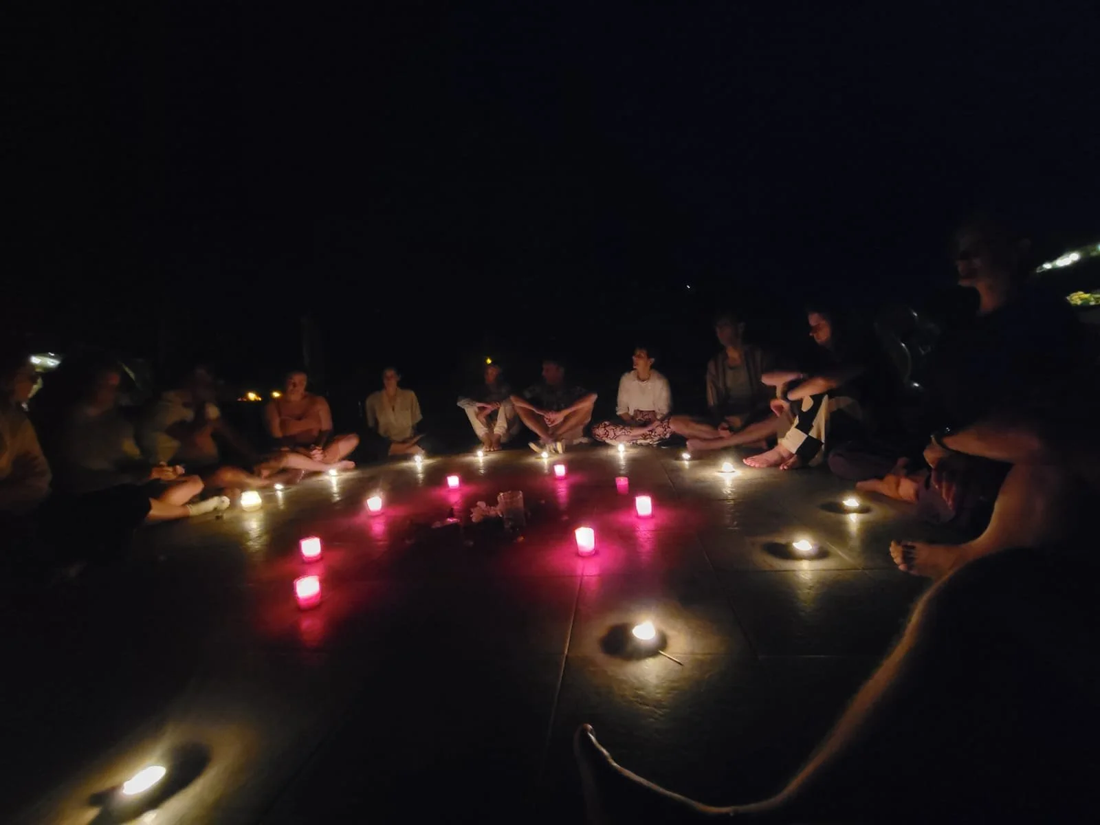 Group of people sitting in a circle around candles at night.