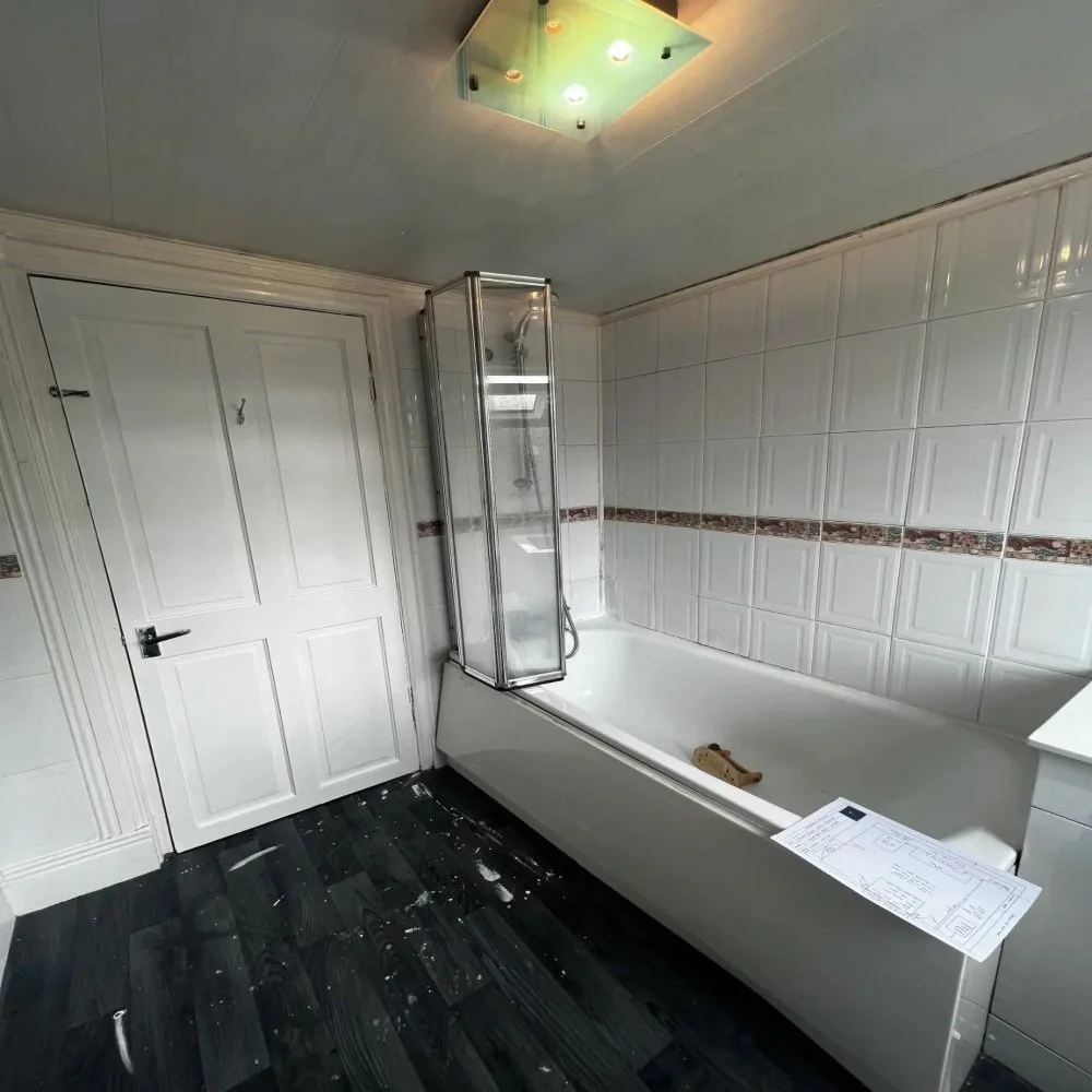 Outdated bathroom in Aigburth featuring a bathtub with glass shower screen, white tiled walls with decorative border, dark flooring, and ceiling light fixture