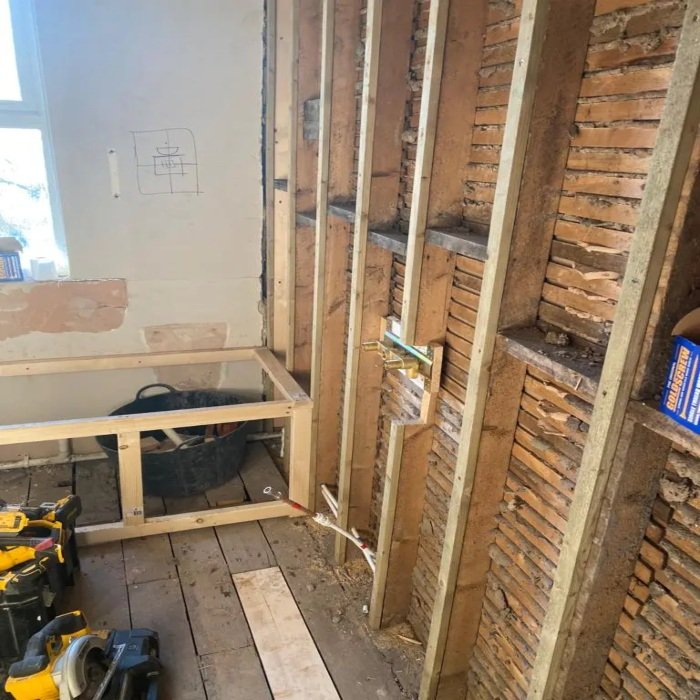 Bathroom renovation in Mossley Hill showing exposed stud wall framing, original lath and brickwork, first fix plumbing for basin, and timber bath frame during early construction stage.
