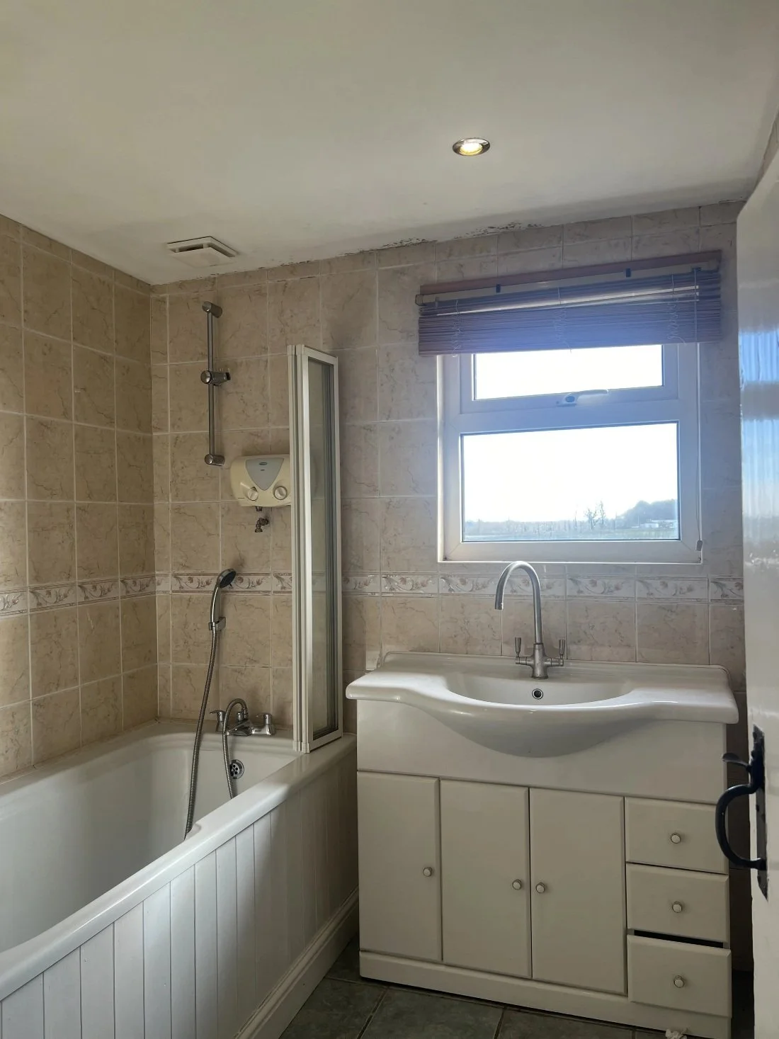 Outdated bathroom with beige wall tiles, bathtub with shower screen and vanity unit prior to renovation in a Halewood home