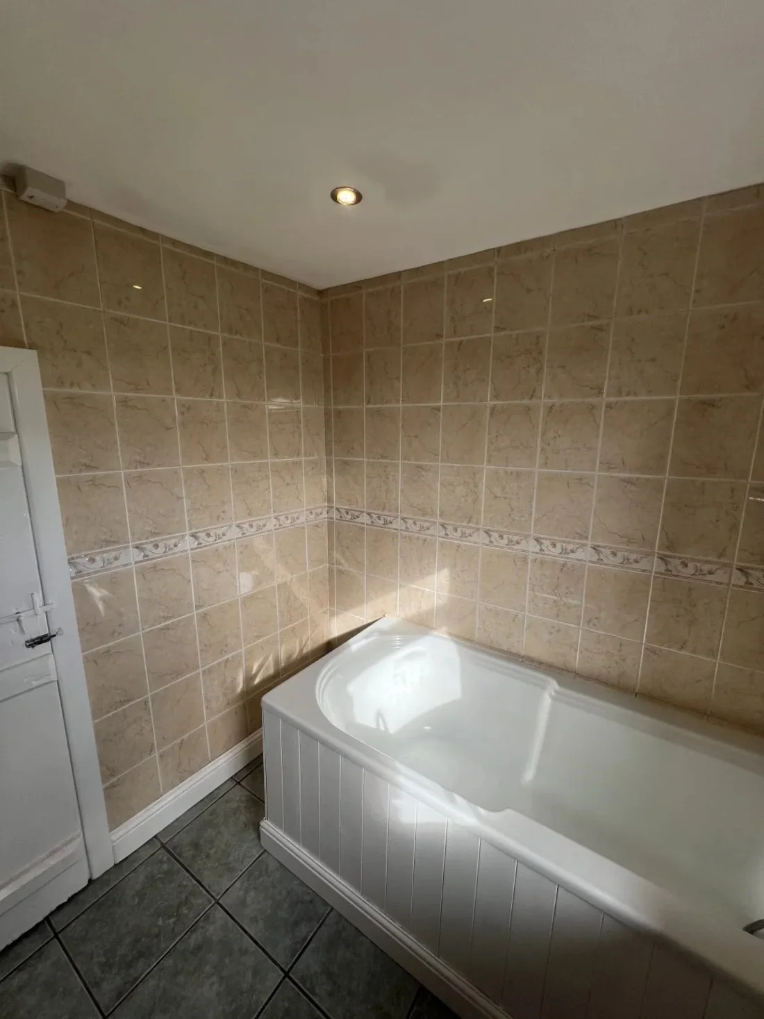 Old bathtub with beige wall tiles and dark floor tiles in a dated bathroom prior to refurbishment in a Halewood home