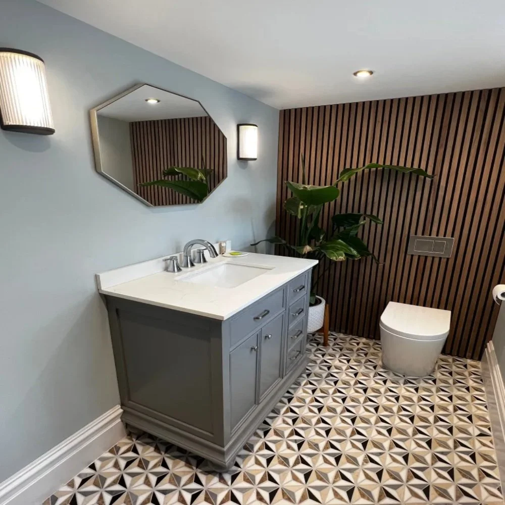 Modern downstairs cloakroom in Allerton featuring a grey vanity unit with chrome tap, octagonal mirror, wall lighting, geometric patterned floor tiles, wood slat feature wall, and contemporary toilet with indoor plant