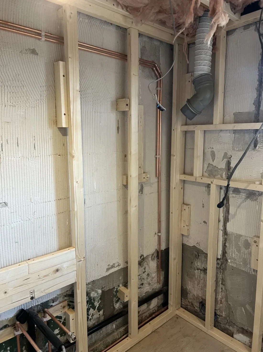 Close-up of bathroom renovation showing timber stud walls, copper pipework and ventilation ducting during first fix stage in a Halewood home
