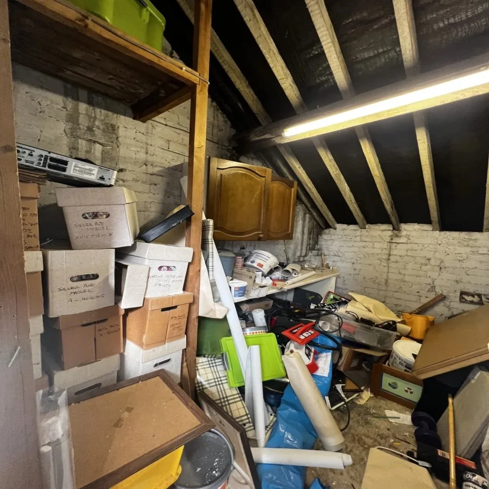 Cluttered loft space with stacked boxes, tools, and old cabinetry being cleared out during the strip-out stage of a bathroom renovation in Bebington