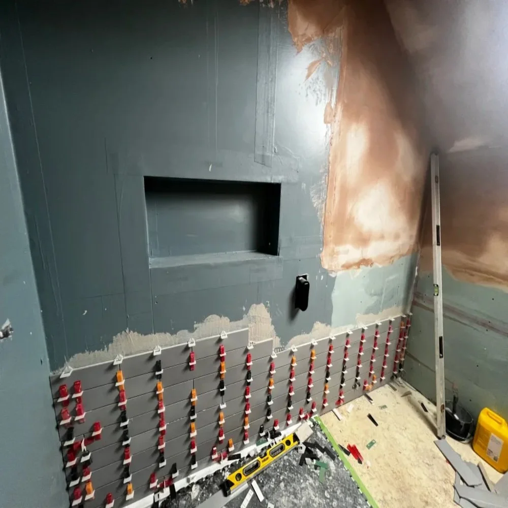 Grey wall tiles being installed with leveling clips beneath a recessed wall niche, showing mid-stage bathroom renovation work in Bebington