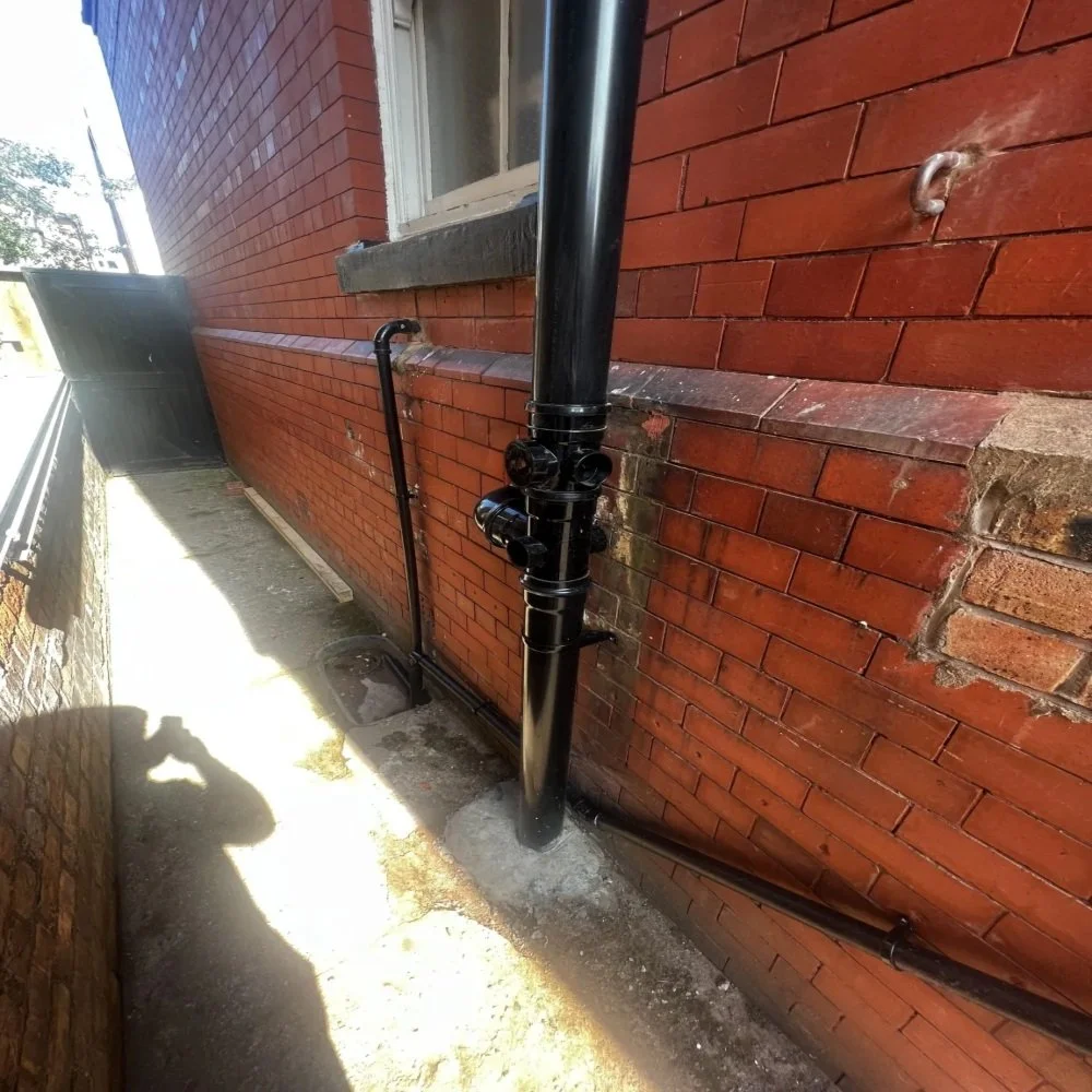 Ground-level view of a Bebington property showing newly installed black soil stack with multiple pipe connections, external drainage runs, and brick wall setting in a narrow side passage