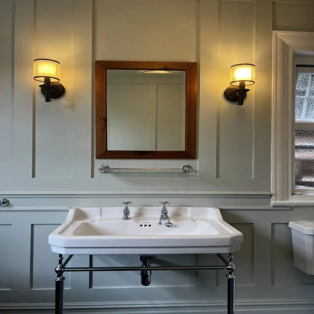 Traditional bathroom in Bebington featuring a wall-mounted ceramic basin with chrome legs, wooden framed mirror, and twin wall lights set against elegant panelled walls