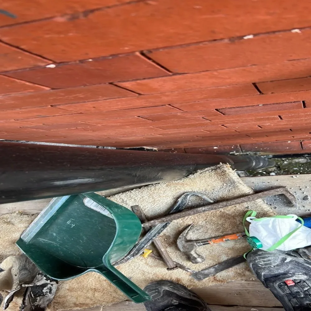 Close-up of bathroom renovation in Bebington showing a black soil pipe running beneath floorboards with tools, debris, and protective equipment visible during installation work