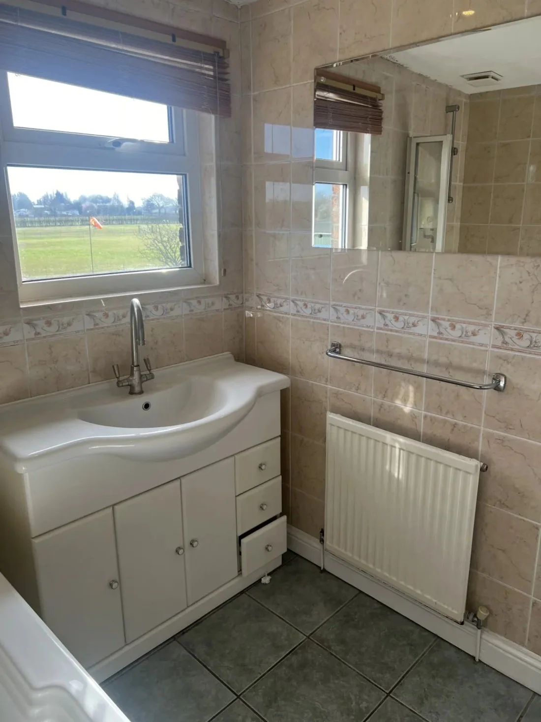 Dated bathroom vanity unit with sink, tiled walls and radiator beneath mirror prior to renovation in a Halewood home