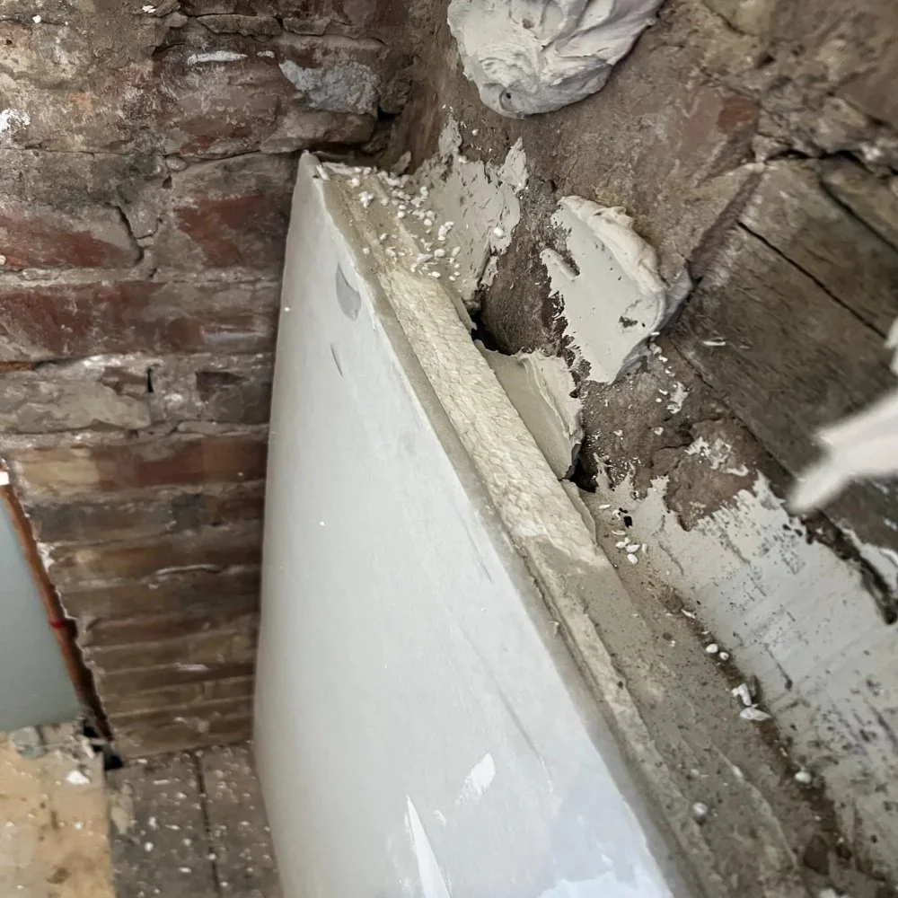 Close-up of bathroom renovation in Bebington showing insulation backer board being fitted against exposed brick wall with adhesive, highlighting preparation work before plastering or tiling