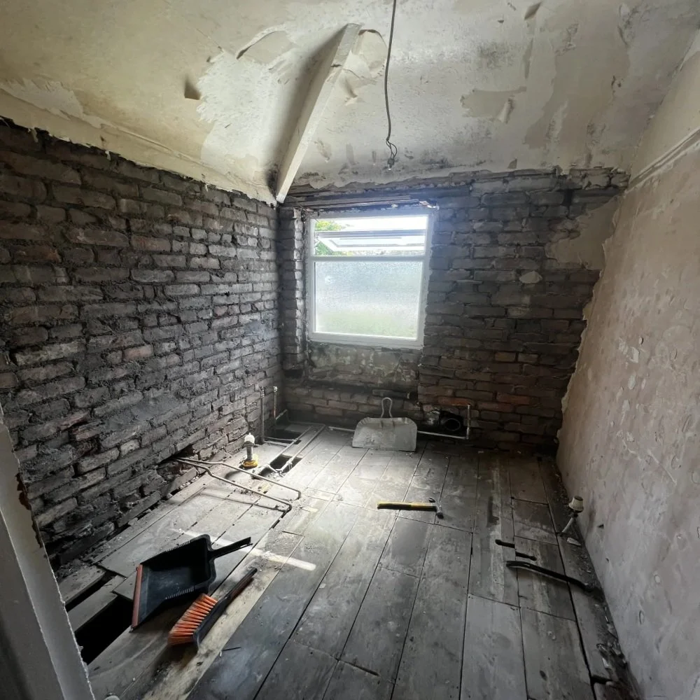 Bathroom renovation in Aigburth during strip-out phase showing exposed brick walls, removed fixtures, timber floorboards, and tools scattered across the room