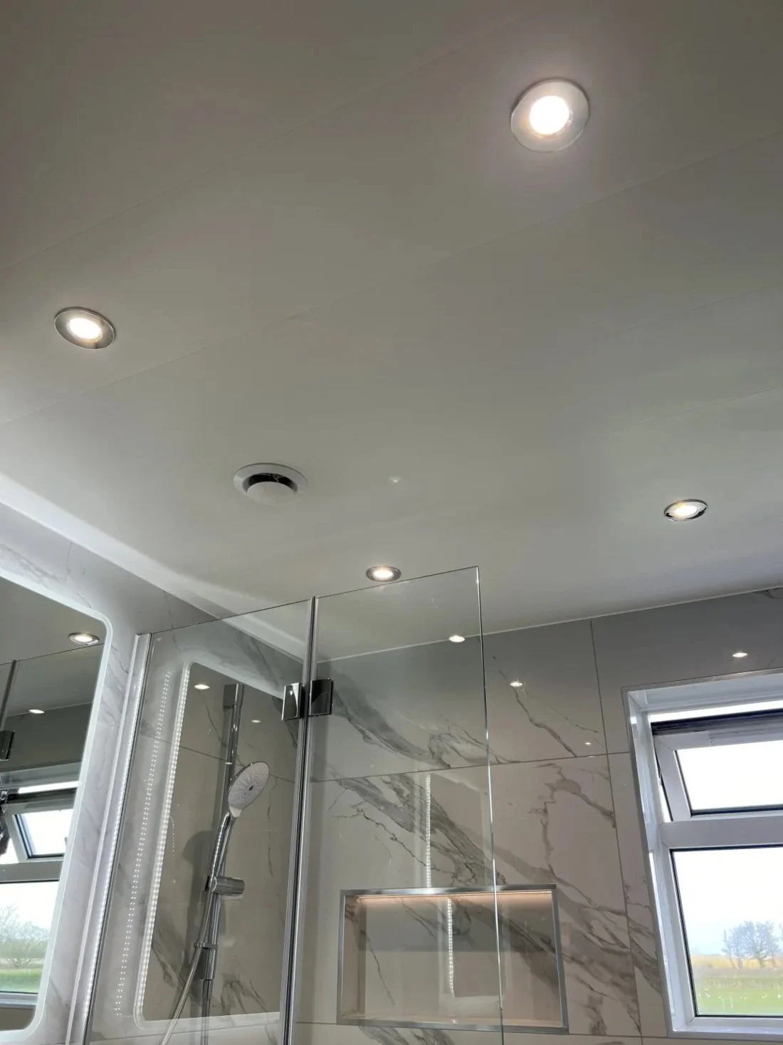 Modern bathroom ceiling with recessed spotlights and extractor fan above marble effect shower area in a Halewood home