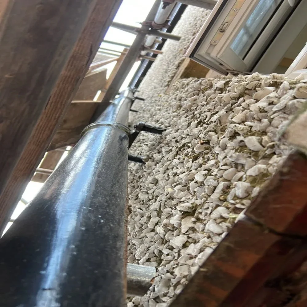 Close-up upward view of newly installed black soil stack pipe fixed to an exterior pebble-dash wall in Bebington, with scaffolding and open window visible during installation work