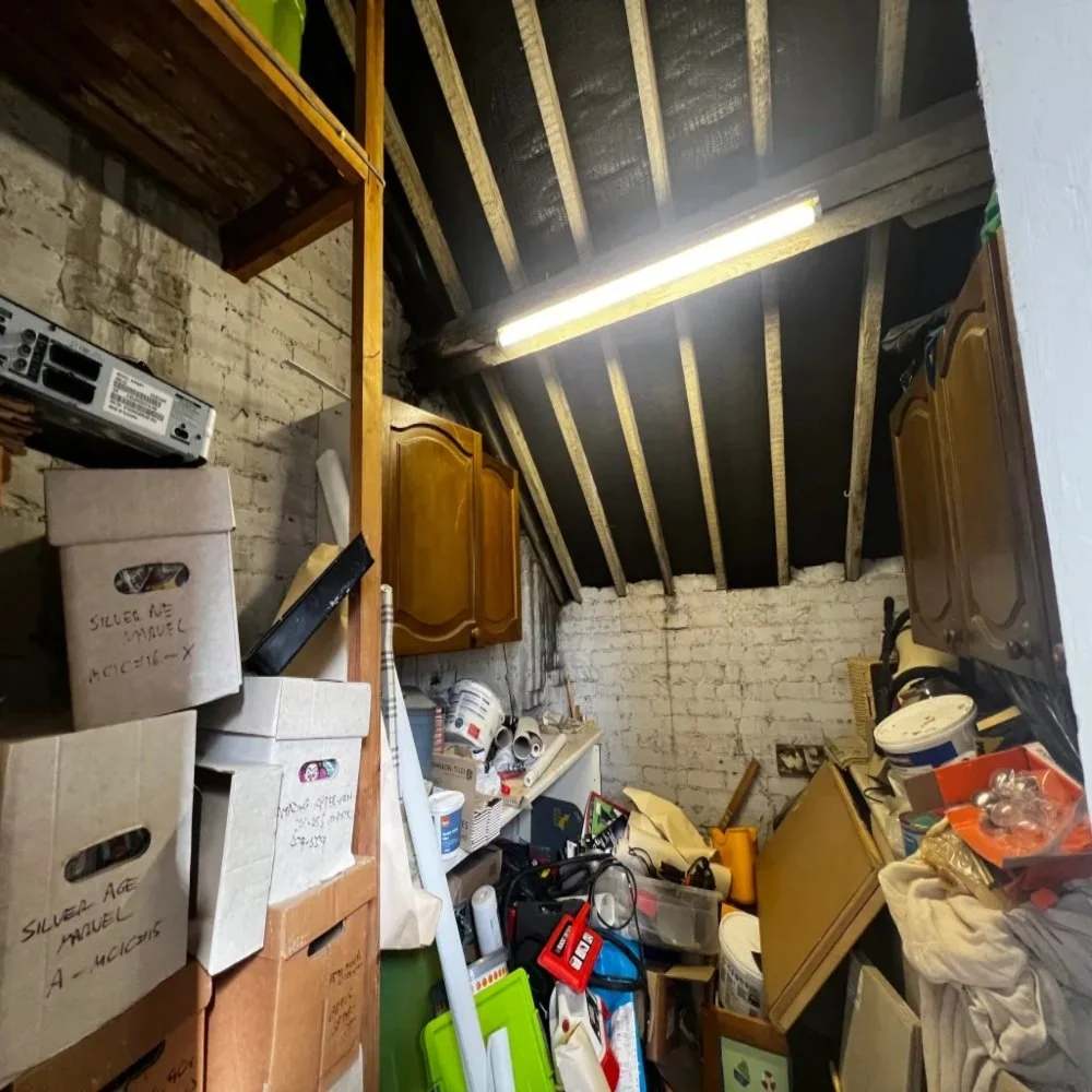 Cluttered loft space with exposed beams, boxes, and old cabinets being cleared as part of a bathroom renovation project in Bebington