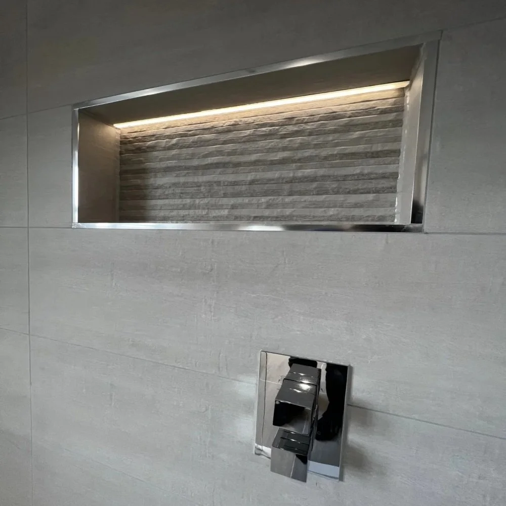 Close-up of a recessed shower niche with LED strip lighting, textured feature tiles, and chrome control valve set within grey tiled wall in a West Derby bathroom renovation