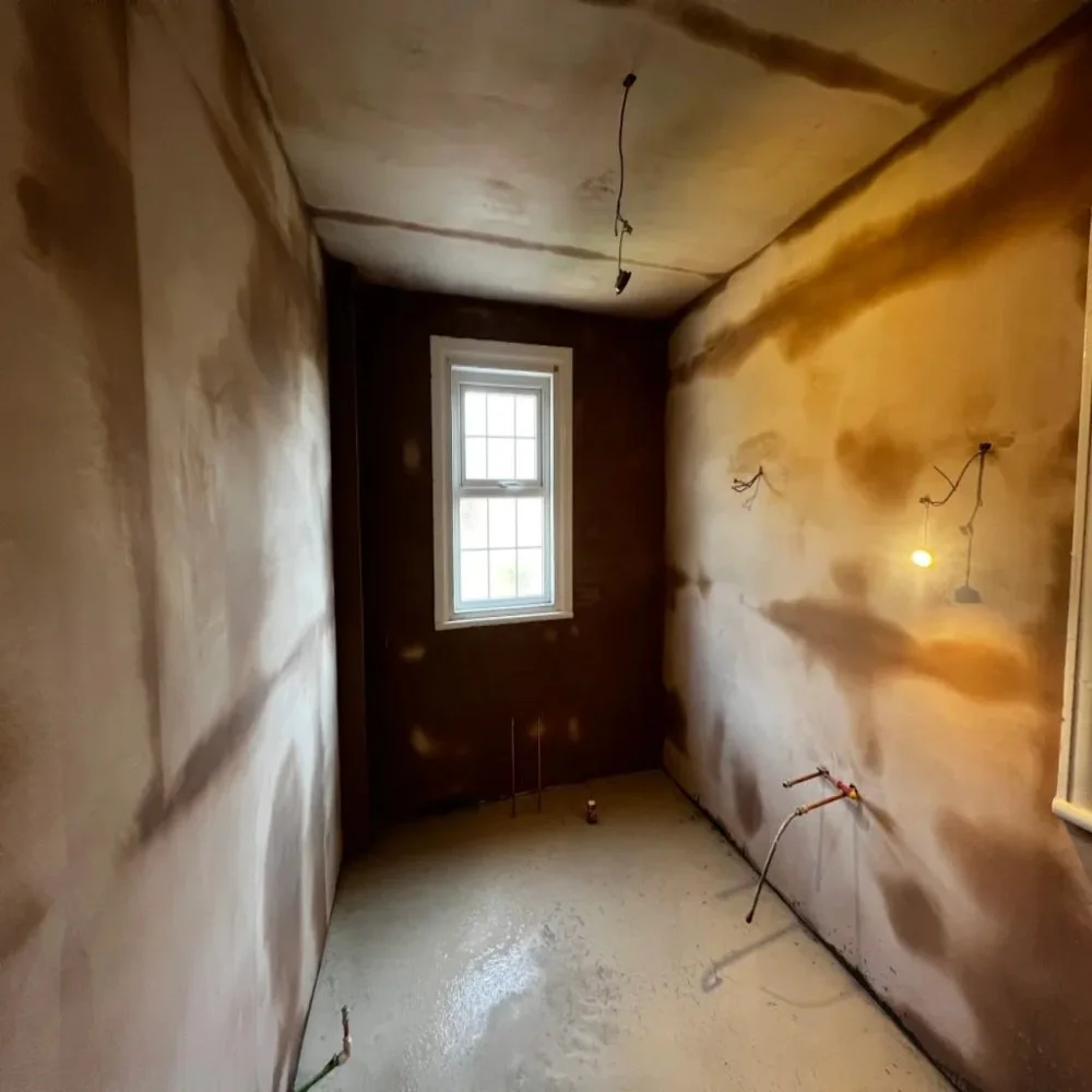 Bathroom renovation in Bebington showing freshly plastered walls, visible drying patches, exposed wiring and pipework, and a newly prepared floor ready for tiling and installation