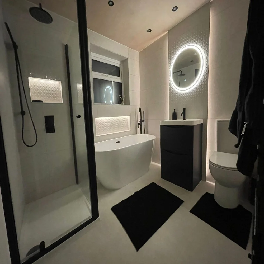 Contemporary bathroom renovation in Cheshire featuring a freestanding bath, walk-in glass shower, round LED mirror, black vanity unit, and soft ambient lighting