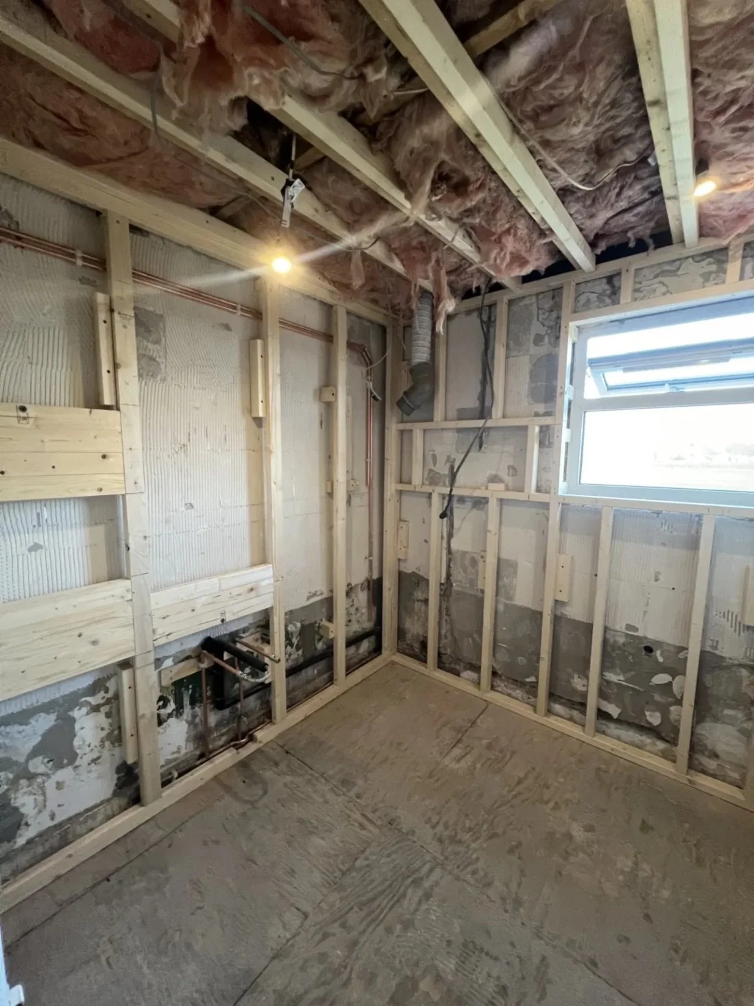 Bathroom renovation in progress showing stripped walls, exposed timber framing, pipework and insulation during first fix stage in a Halewood home