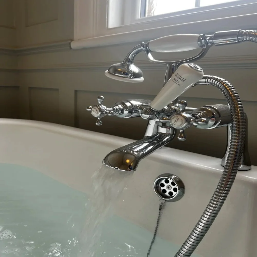 Close-up of a freestanding bath in Bebington with chrome mixer taps, handheld shower attachment, and running water filling the tub against classic panelled walls