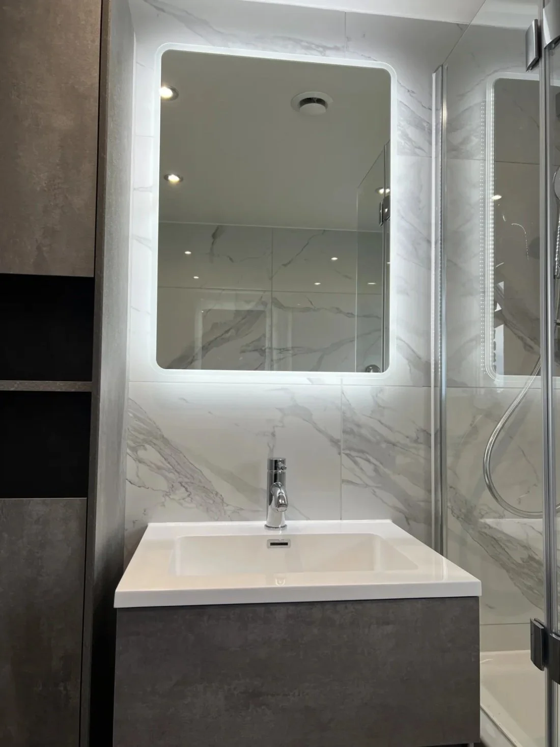Modern bathroom featuring wall hung vanity unit with basin, illuminated LED mirror and marble effect wall panels in a Halewood home