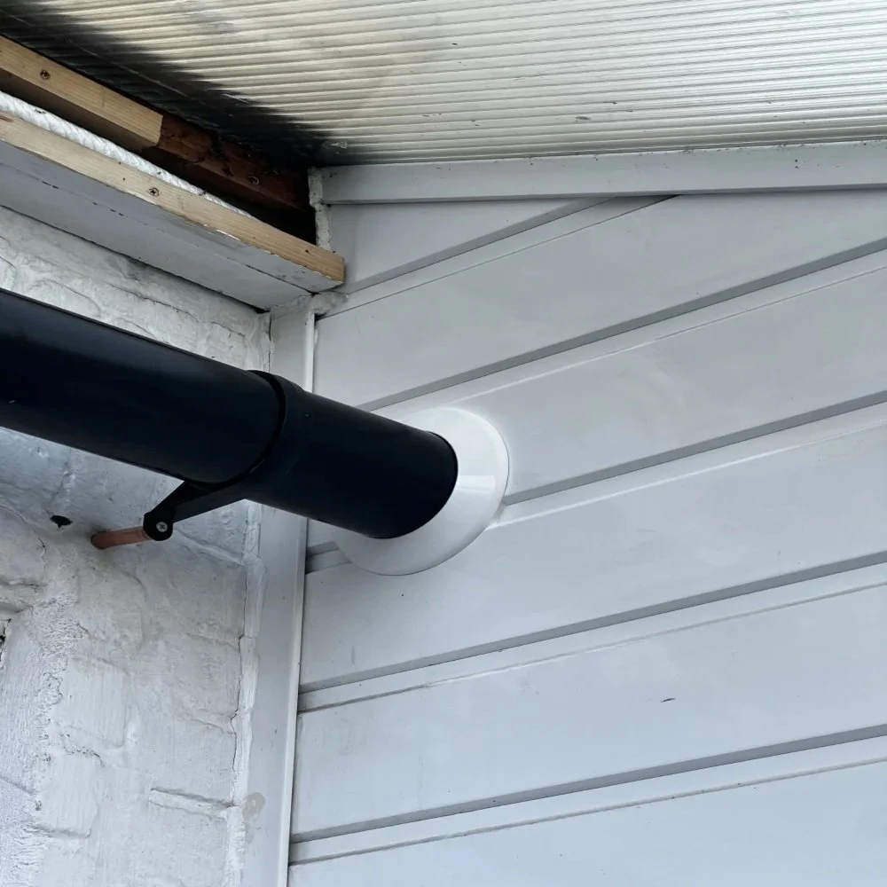 Close-up of newly installed black waste pipe exiting wall with white surround, mounted against exterior cladding and brickwork in Aigburth renovation