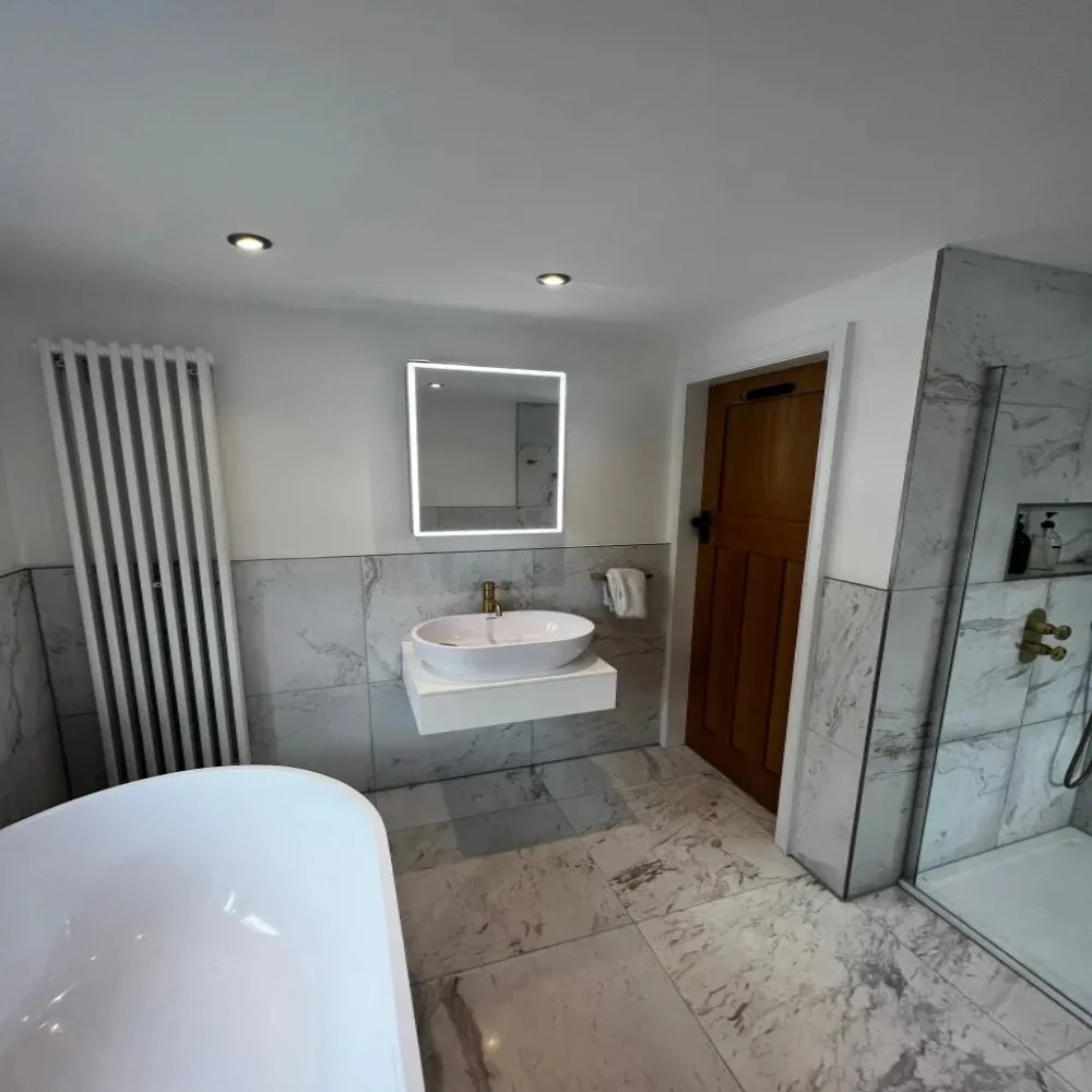 Contemporary main bathroom in Allerton featuring a freestanding bath, marble effect tiles, walk-in glass shower with brass fixtures, floating vanity with vessel basin, LED mirror, and vertical radiator
