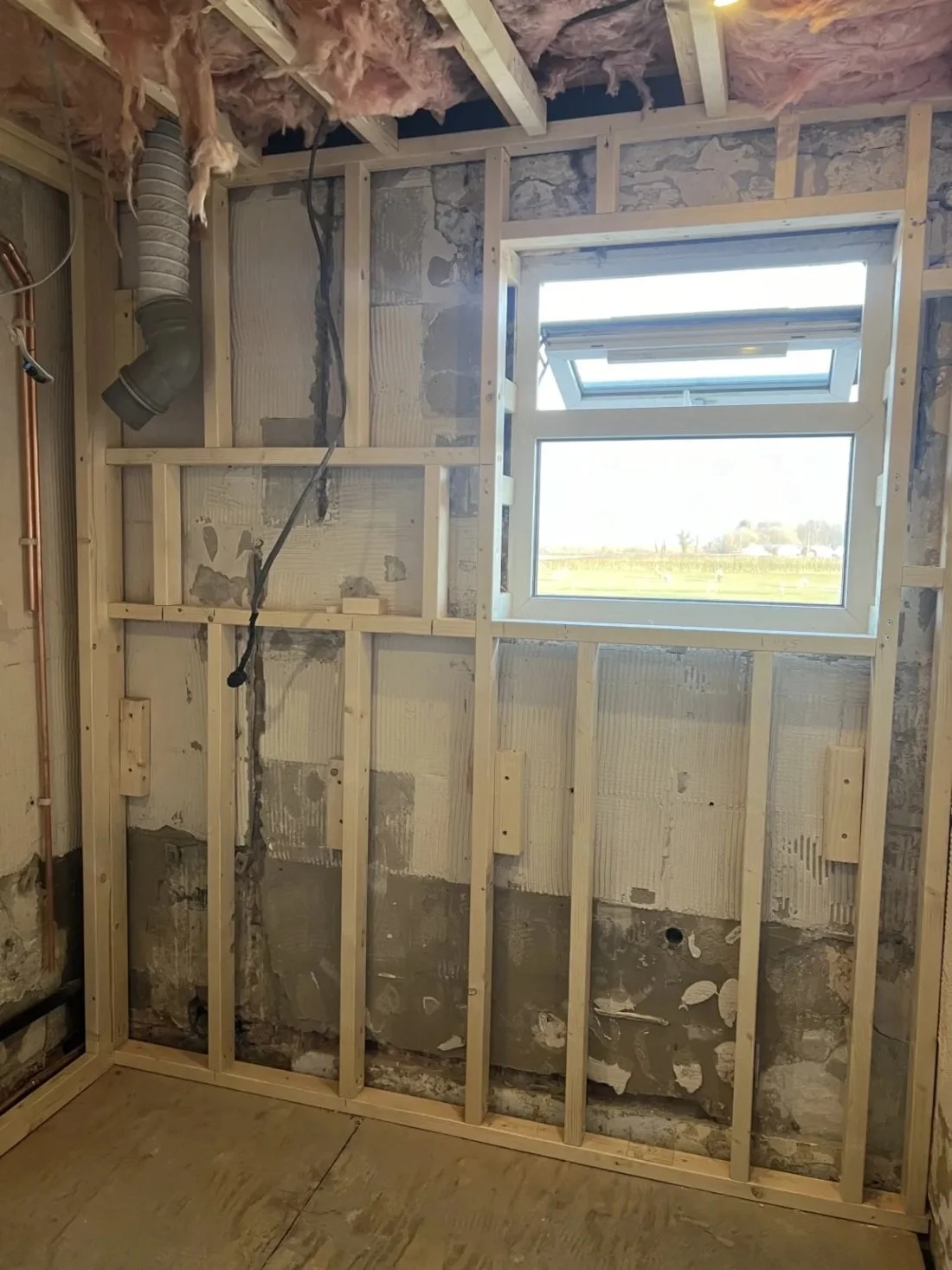Bathroom renovation showing timber stud wall framing, exposed pipework and window during construction phase in a Halewood home