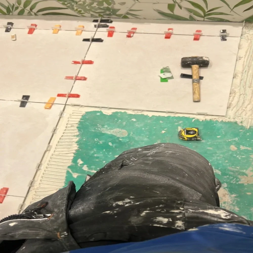 Large format bathroom floor tiles being installed with spacers and leveling clips, tools visible during renovation in Edge Hill
