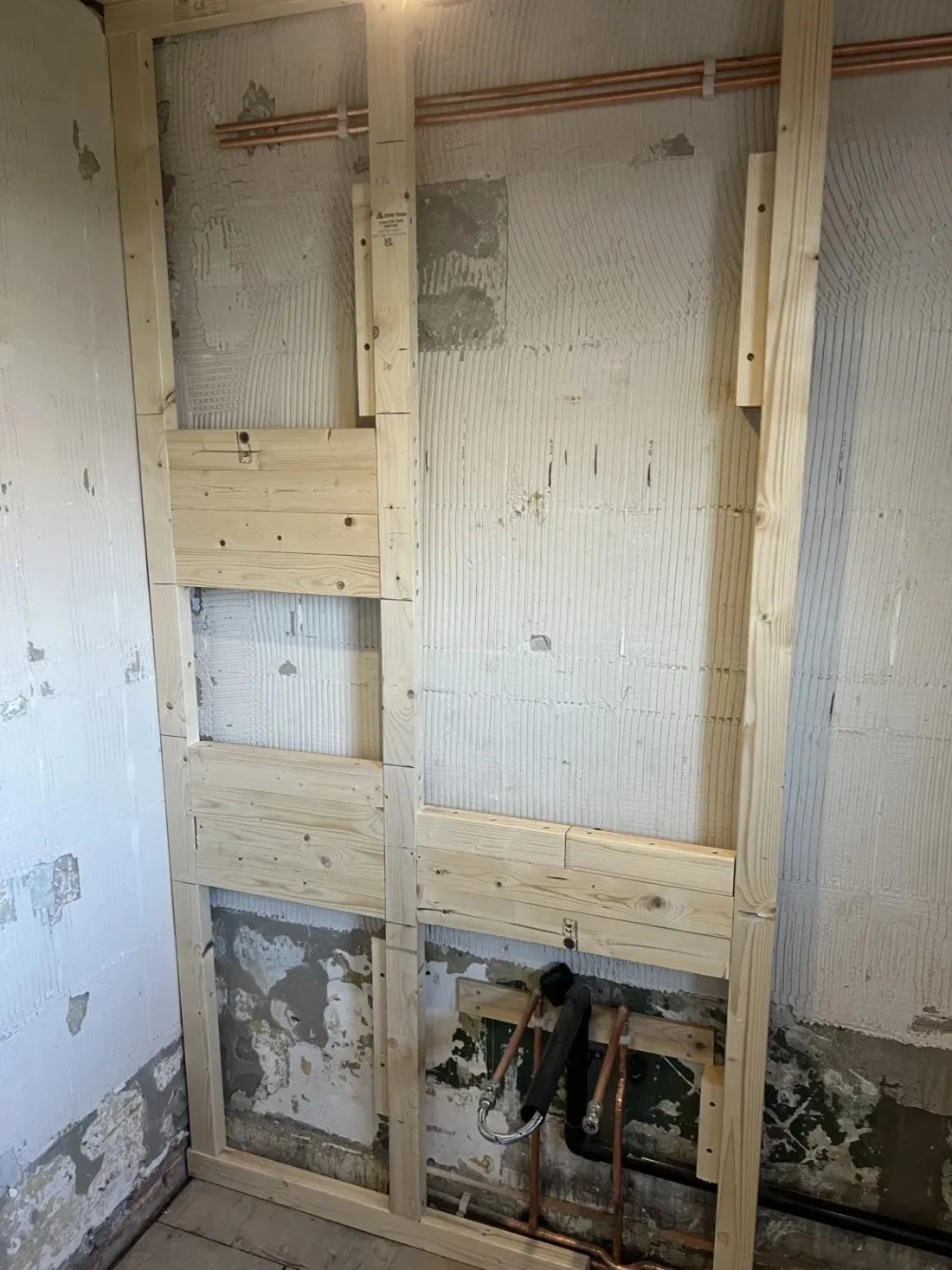 Timber stud wall framework with exposed plumbing pipes prepared for bathroom installation during renovation in a Halewood property