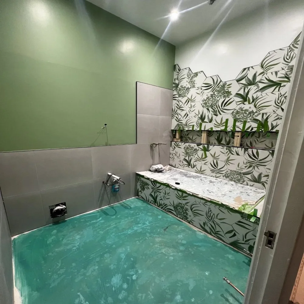 Bathroom renovation in Edge Hill showing green painted walls, partial tiling and decorative leaf feature wall during installation stage