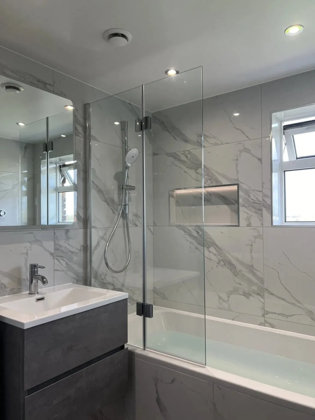 High-end bathroom featuring marble effect wall panels, bath with glass screen, recessed shelf and modern vanity unit in a Halewood home