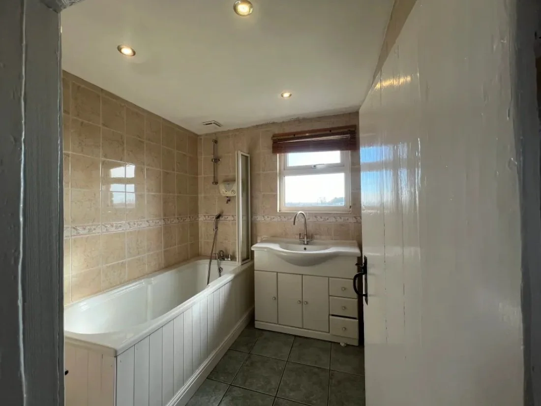 Full view of dated bathroom with bathtub, beige tiles and vanity unit before modern renovation in a Halewood property