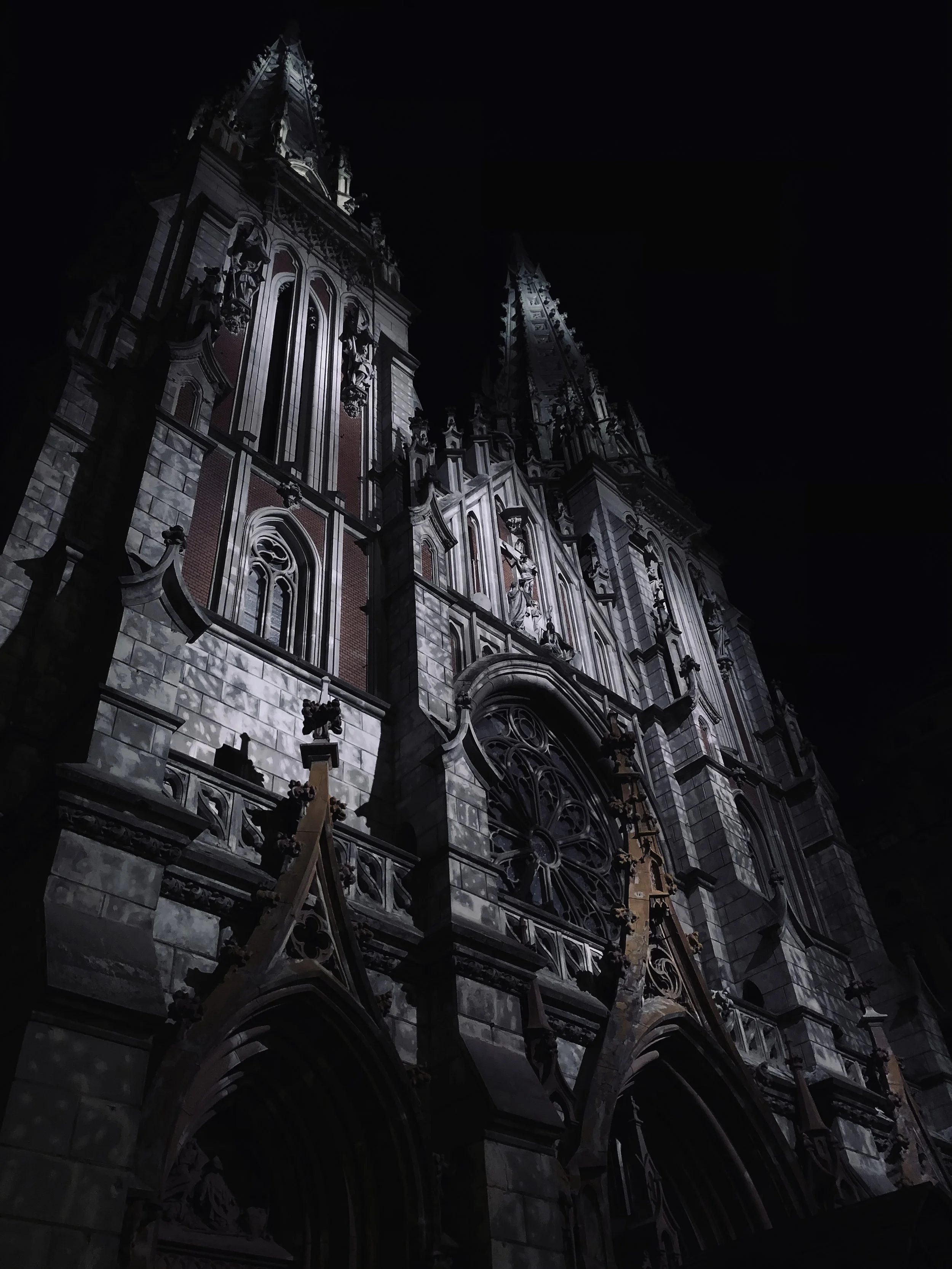 A Gothic-style cathedral at night with illuminated ornate architectural details and large stained glass windows.