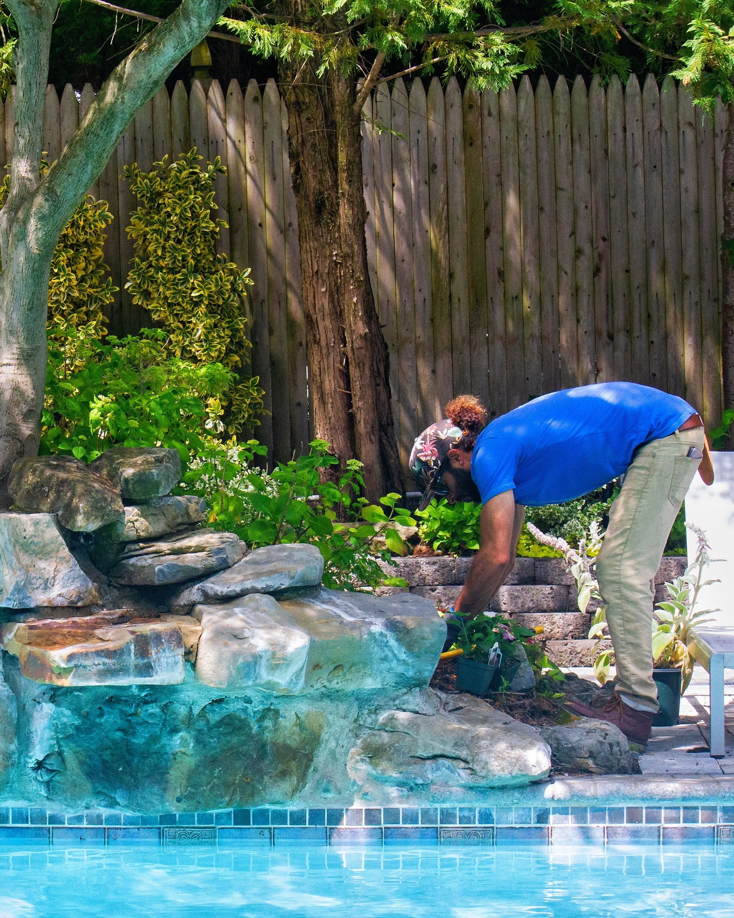 Pool landscaping with natural rock waterfall and lush planting design creating a backyard oasis — landscape design by Chasky, Lawrence NY