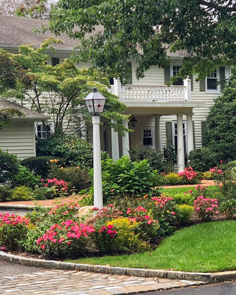 Colorful lush front yard and driveway planting design creating stunning curb appeal — landscape design by Chasky, Woodbury NY