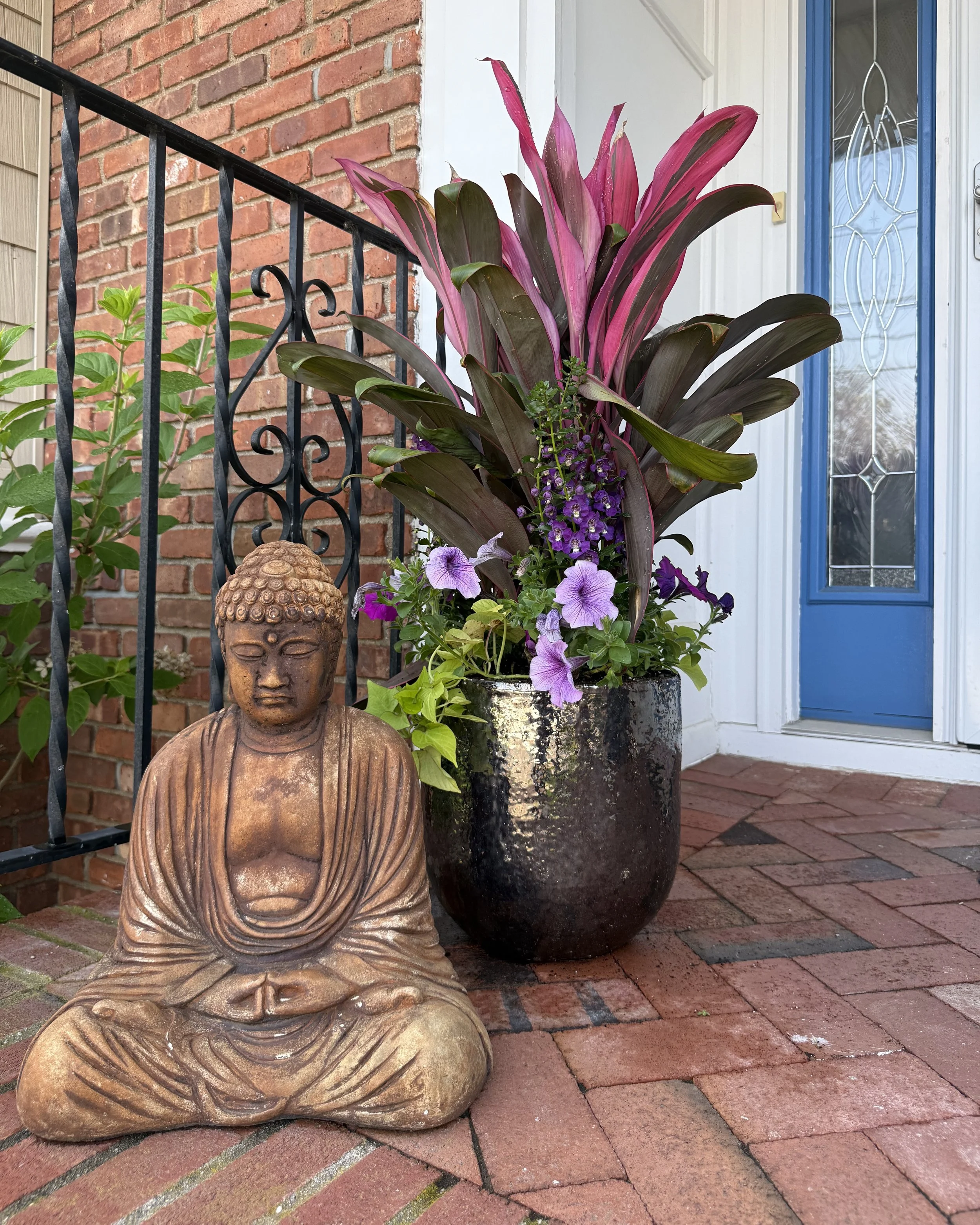Tropical cordaline with purple flowers and lush green leaves in custom entrance planter pot with buddha accent — landscape design by Chasky, Long Beach NY